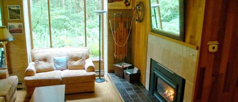 Un salón acogedor con chimenea, un sofá y un ventanal que ofrece vistas a zonas verdes.