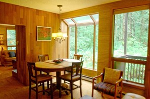 Enjoy meals in a warm dining area with a forest view, surrounded by comfortable seating and natural light.