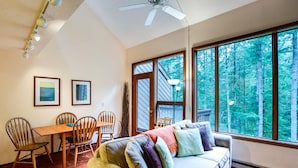 A cozy room with a large window, a ceiling fan, a dining table with chairs, and a sofa with cushions. - Snowater Condo #85 - Deluxe two Story Condo! (Deming)