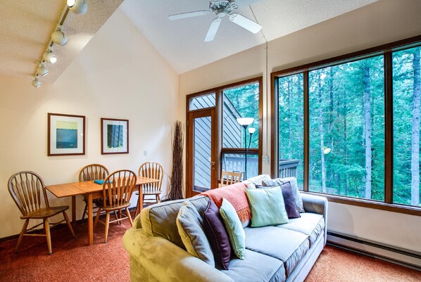 A cozy room with a large window, a ceiling fan, a dining table with chairs, and a sofa with cushions. - Snowater Condo #85 - Deluxe two Story Condo! (Deming)