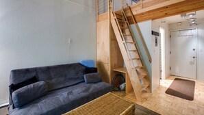 Um quarto com um sofá cinzento, uma escada de madeira e uma porta branca.