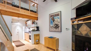 Uma sala de estar espaçosa com pé direito alto, escada de madeira, cozinha e lareira.
