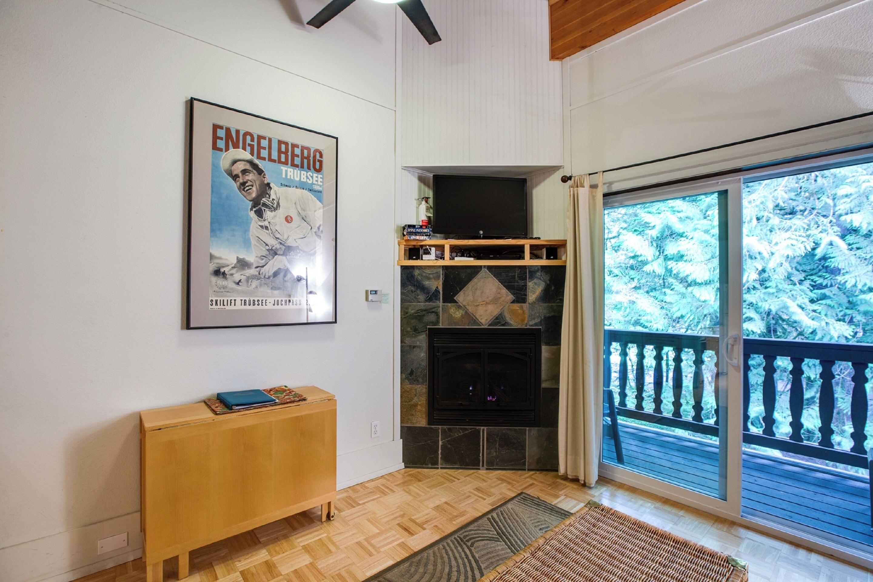 A living room with a fireplace, a television, a wooden bench, and a large poster on the wall.
