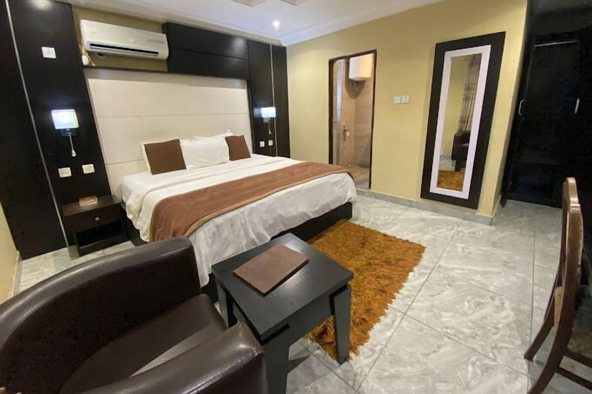 A modern hotel room with a large bed, a desk, a chair, and a mirror.