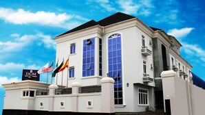 A large, white building with multiple flags, including the American flag, and a sign that reads "DCM Hotel." - DCM Hotel and Suites (Lagos)