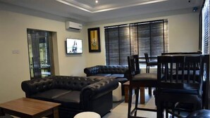 A modern living room with a sectional sofa, a dining table, and a bar area. - DCM Hotel and Suites (Lagos)