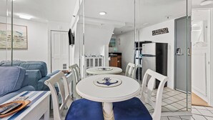 Un salon moderne comprenant un canapé, une table à manger, des chaises et un coin cuisine visible à travers une cloison en verre.