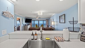 Une cuisine moderne dotée d’un grand îlot central, d’un coin repas offrant une vue agréable et d’un salon équipé d’un ventilateur de plafond.