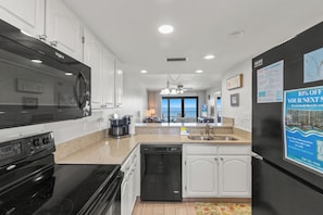 A modern kitchen with a black stove, white cabinets, a dishwasher, and a refrigerator.