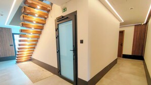 A modern hotel lobby with a wooden staircase, a reception area, and a door with an emergency exit sign. - King Studio 2 (Leiria)
