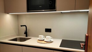 A modern kitchen with a microwave, a sink, and a countertop with two white cups and a plate. - King Studio 2 (Leiria)
