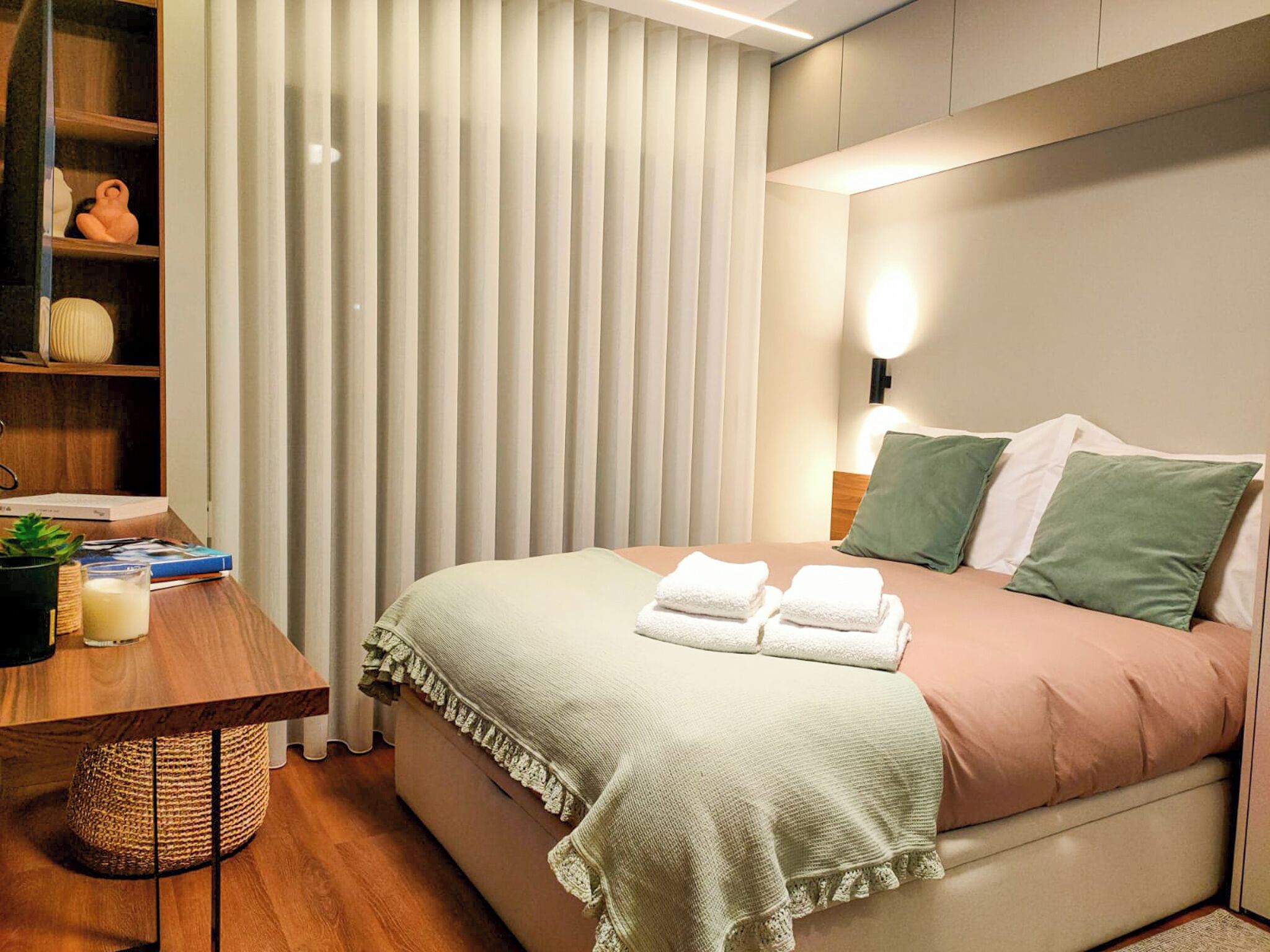Habitación de hotel moderna con una cama bien hecha, una mesita de noche con lámpara y una estantería.