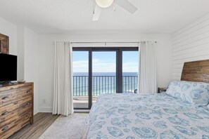 Ein Schlafzimmer mit einem großen Bett, einem Schminktisch, einem Fernseher und einem Balkon mit Meerblick.