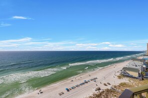 Ein Strand mit einer Reihe von Liegestühlen und Sonnenschirmen, ein Gebäude mit geneigtem Dach und dem Ozean im Hintergrund.