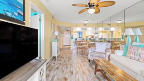 A spacious living area with a large flat-screen TV, a ceiling fan, and a dining area with chairs and a table.