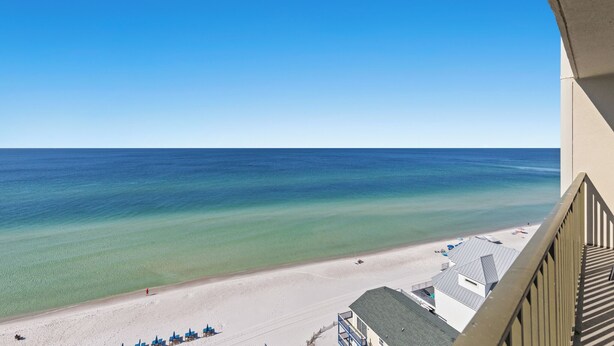 A beach view from a balcony with clear skies, a sandy beach, and a calm sea.