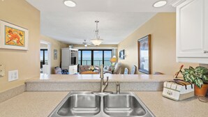 A kitchen with a double sink, a ceiling fan, and a view to the living area.