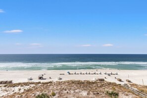 Een strand met een rij strandparasols en ligstoelen, een wachthuisje en een zandvlakte met weinig begroeiing.