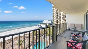 A balcony with a view of the beach and ocean, two chairs, and a small pool.