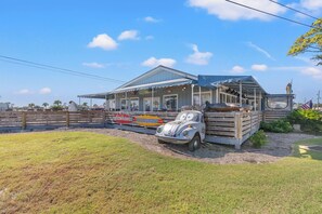 A restaurant with a covered outdoor seating area, a vintage car, and a wooden fence.