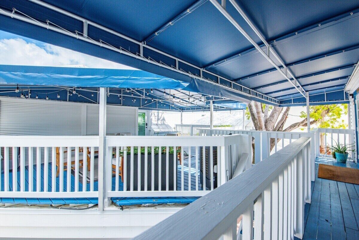 Um deck externo coberto, com corrimãos brancos e um toldo azul.