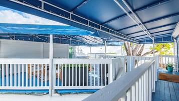 Um deck externo coberto, com corrimãos brancos e um toldo azul.