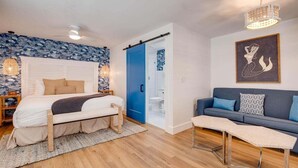 A bedroom with a bed, a bedside table, a blue door, a sofa, and a wall with a mermaid painting.
