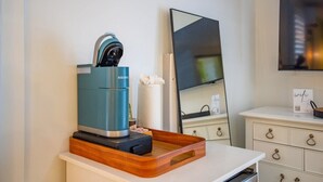 A kitchenette with a coffee maker, a mirror, and a tray on a white countertop.