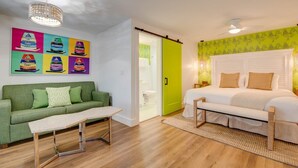 A room with a green sofa, a white bed, a wooden bench, and a colorful wall art piece.