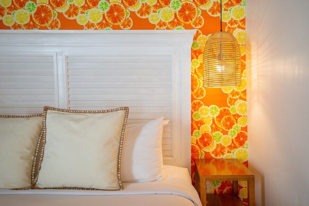 A bedroom with a bed, white headboard, and a wall with a citrus fruit pattern.
