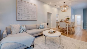 A modern living room with a large sofa, a round coffee table, and a dining area with a wooden table and chairs.