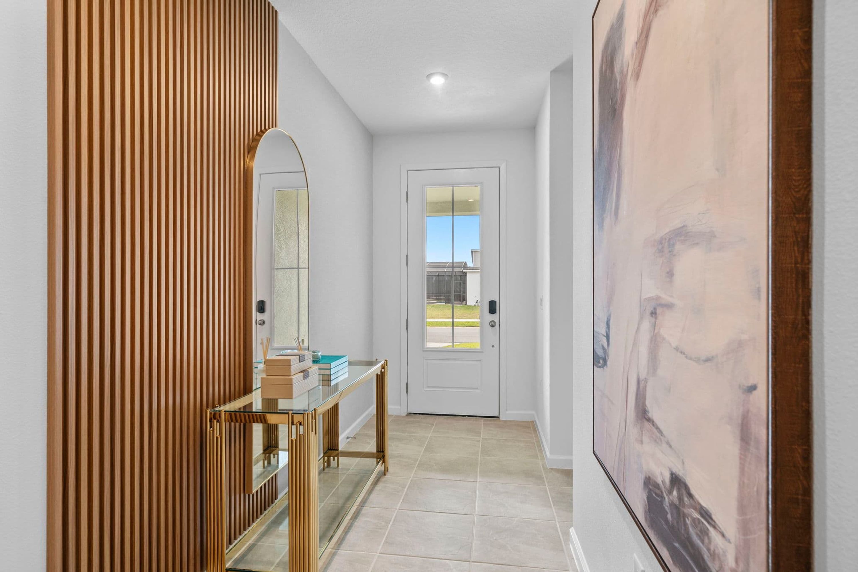A hallway with a wooden panel wall, a glass table with a mirror, and a door with a view of the outside.