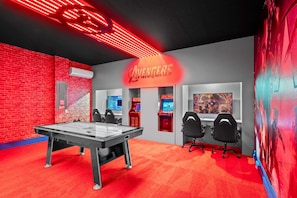 A gaming room with a pool table, gaming stations, and a large Avengers-themed sign.