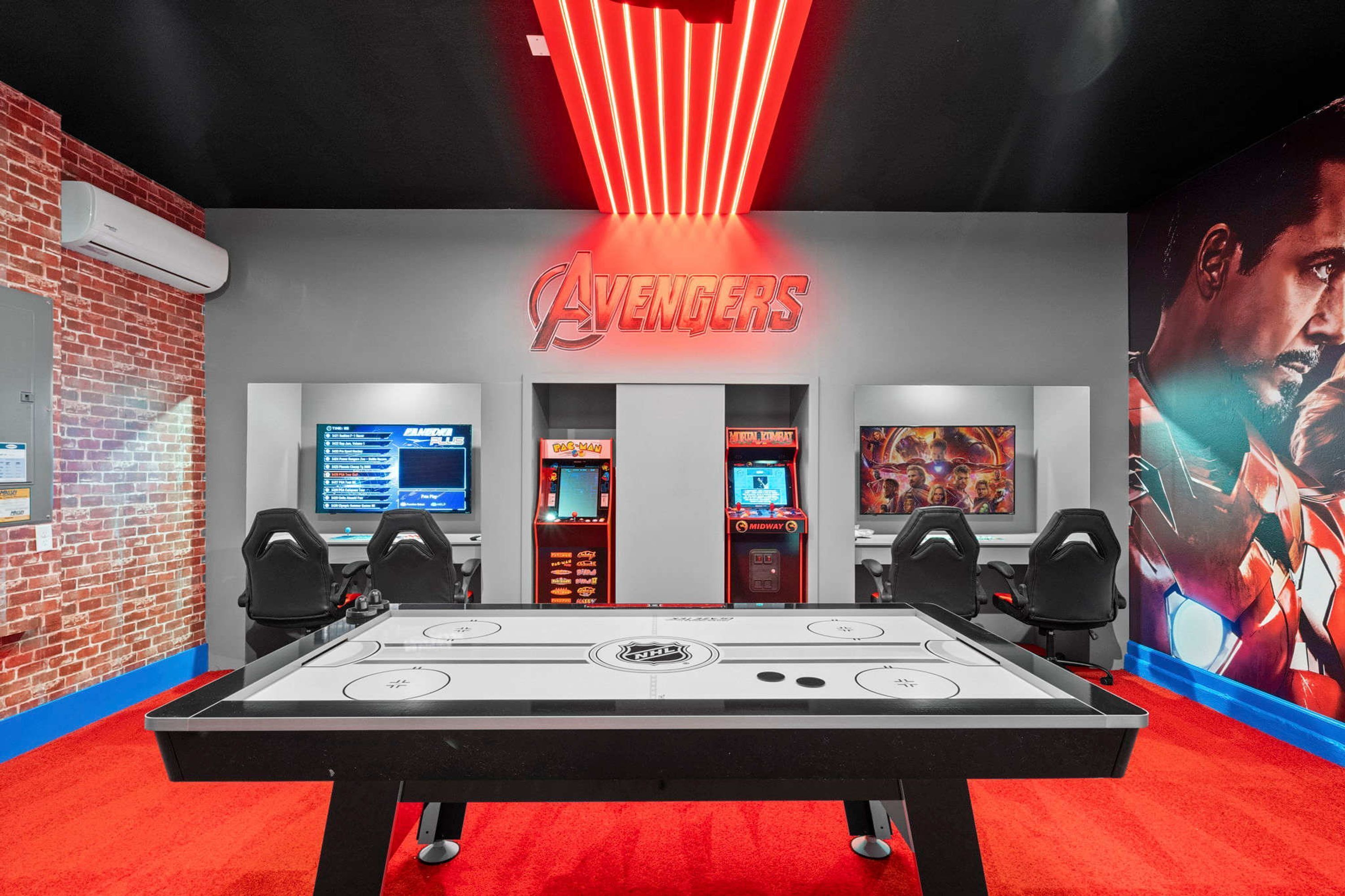 A gaming room with a foosball table, two arcade machines, and a large Avengers poster on the wall.