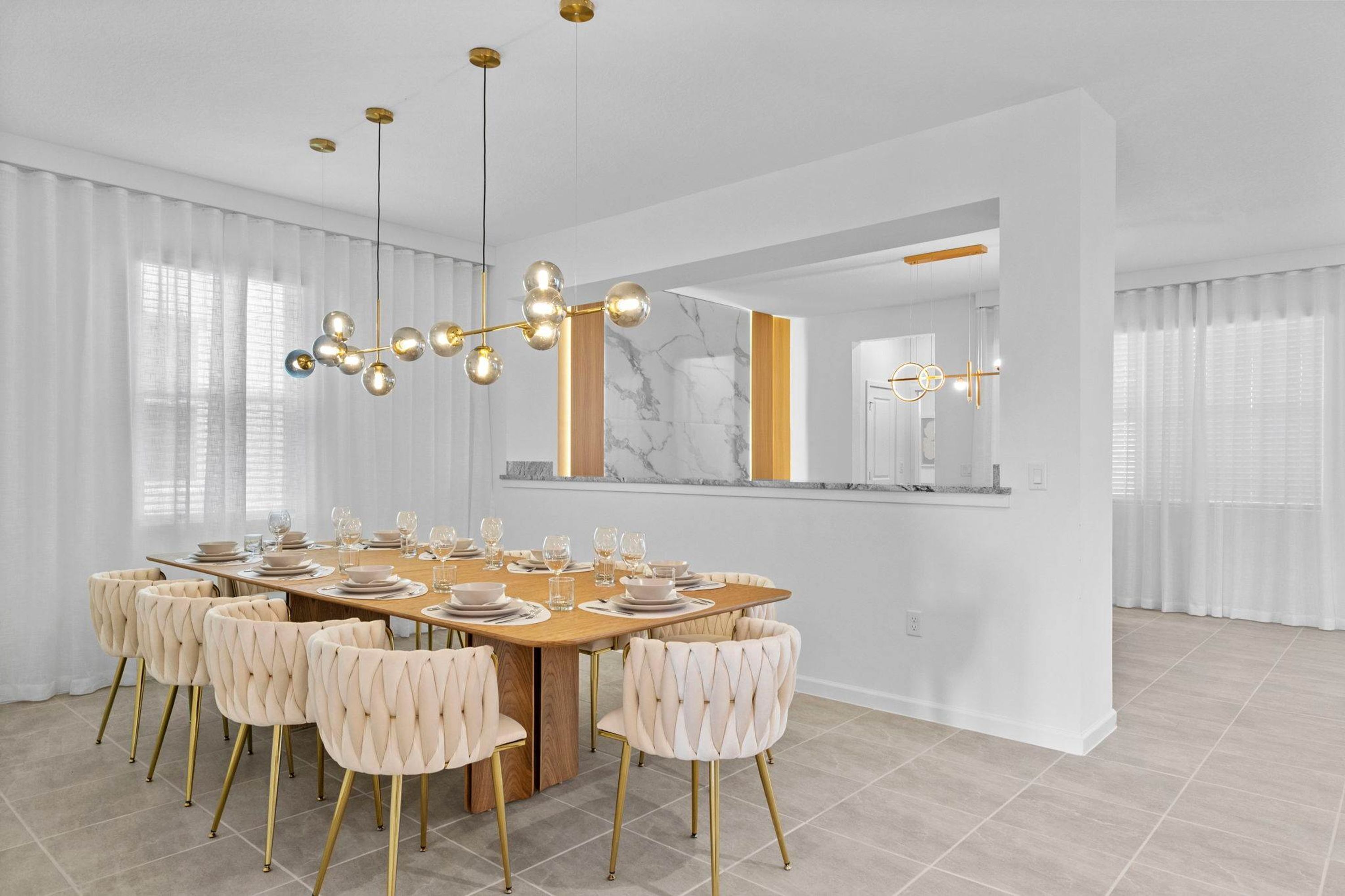 Un comedor moderno con una mesa de madera preparada para seis personas, rodeada de sillas tapizadas con patas doradas.