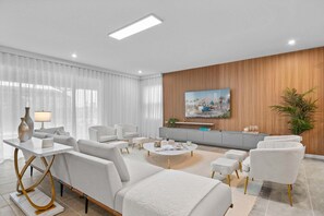 A modern living room with white sofas, a coffee table, and a TV mounted on a wooden wall.