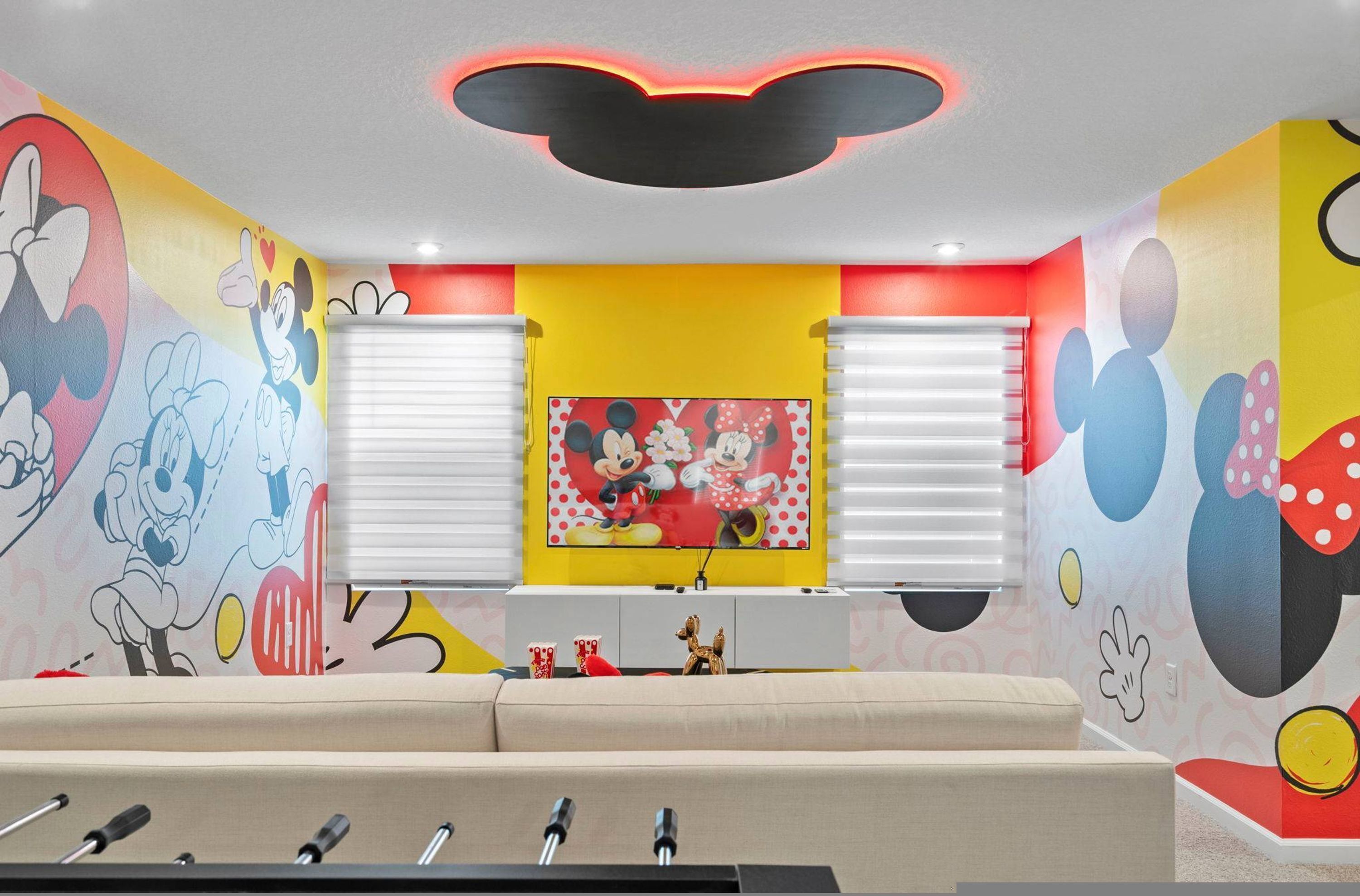 A room with a colorful mural, a sofa, and a table with a Mickey Mouse-themed picture.