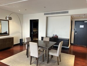 A modern dining area with a rectangular table and six chairs, a dark wooden floor, a large mirror, and a dark door.
