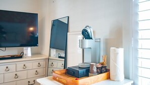 Quarto de hotel com televisão de tela plana, espelho, cafeteira, bandeja com xícaras e um rolo de papel higiênico.