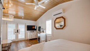 Quarto com cama, escrivaninha, televisão e ventilador de teto.
