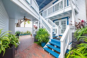 A multi-level wooden staircase with white railings and blue steps, surrounded by potted plants and a brick pathway. - Feather Queen at Custom House Inn | Two Vibrant Suites! (Key West)