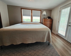 A bedroom with a bed, dresser, lamp, and a door with a view. - Wine Country Finger Lakes Escape - Waneta Lake (Hammondsport)