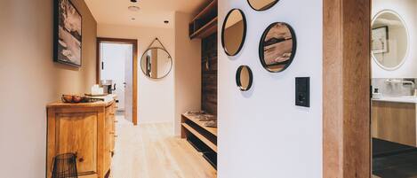 A hallway with wooden flooring, a wooden cabinet with a basket, and a mirror on the wall.