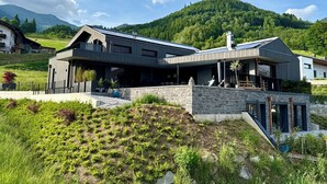 A modern house with a stone facade, large windows, and a balcony overlooking a green hillside. - Apartment Alpinero 405 by we rent (Piesendorf)