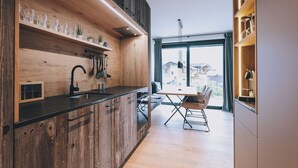 A modern kitchen with wooden cabinets, a black countertop, and a dining area with a table and chairs. - Apartment Alpinero 405 by we rent (Piesendorf)