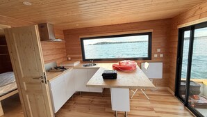A compact kitchen with a large window offering a view of the water, wooden walls, and a small dining area. - Panoramic electric boat, sail on the Lac du Der without a license. Nemours (Éclaron-Braucourt-Sainte-Livière)