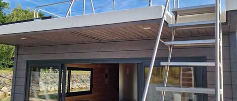 A modern outdoor deck with a glass enclosure, a wooden bench, and a metal staircase.