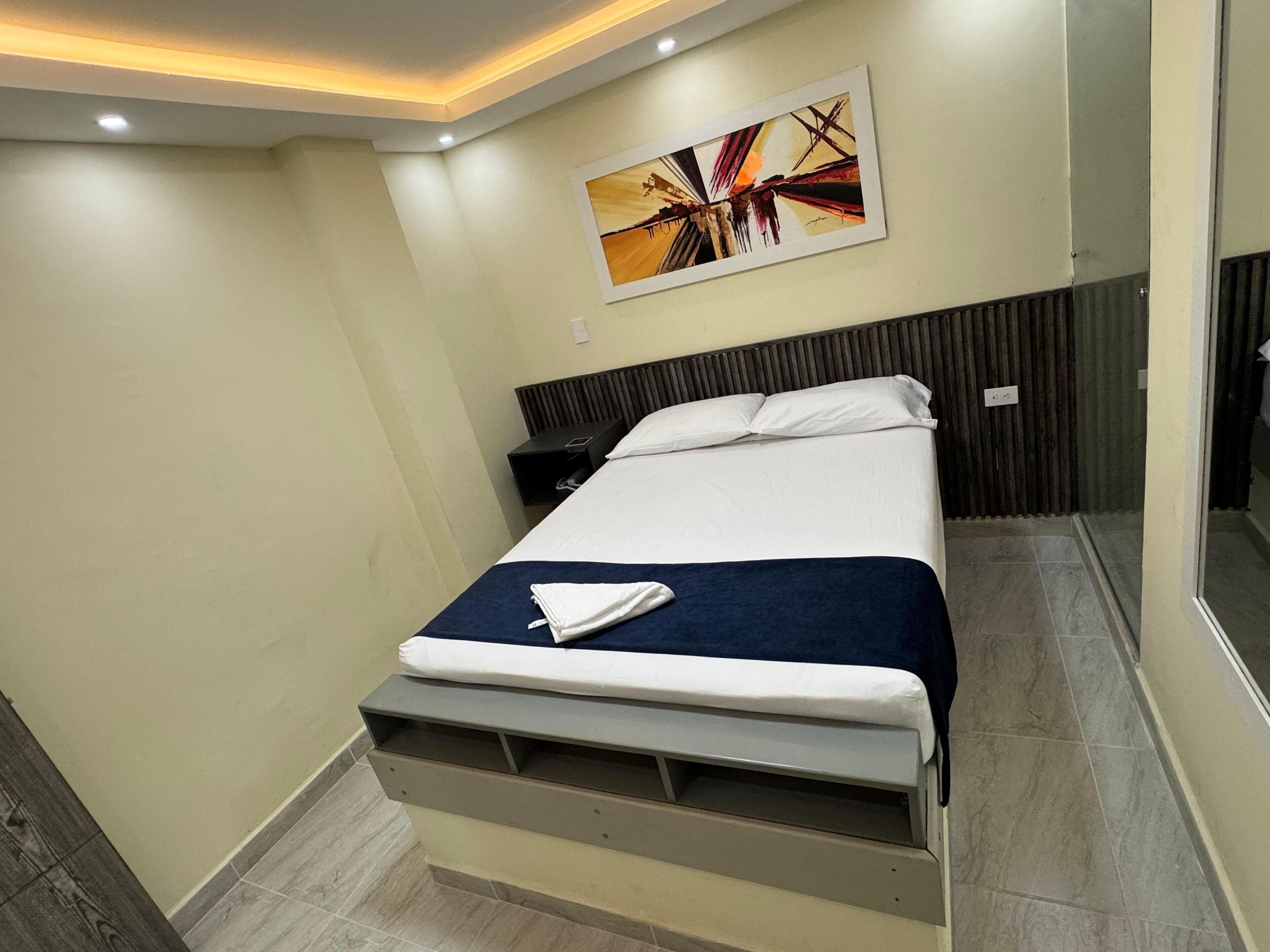 A modern hotel room with a bed, bedside table, and a large mirror.