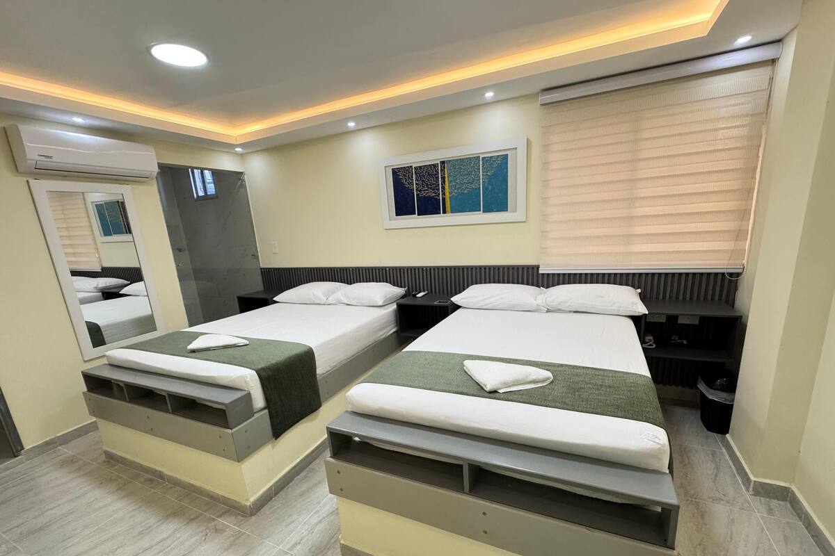 A hotel room with two beds, a large mirror, a painting on the wall, and an air conditioning unit.