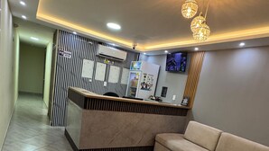 A modern reception area with a reception desk, a sofa, and a small wooden stool. - HOTEL MAGISTRAL SUITER (Quibdó)